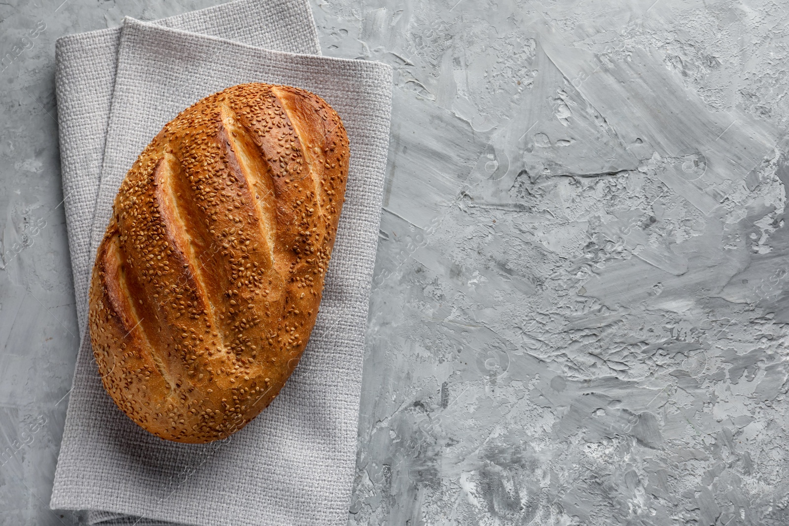 Photo of Freshly baked bread with seeds on grey table, top view. Space for text