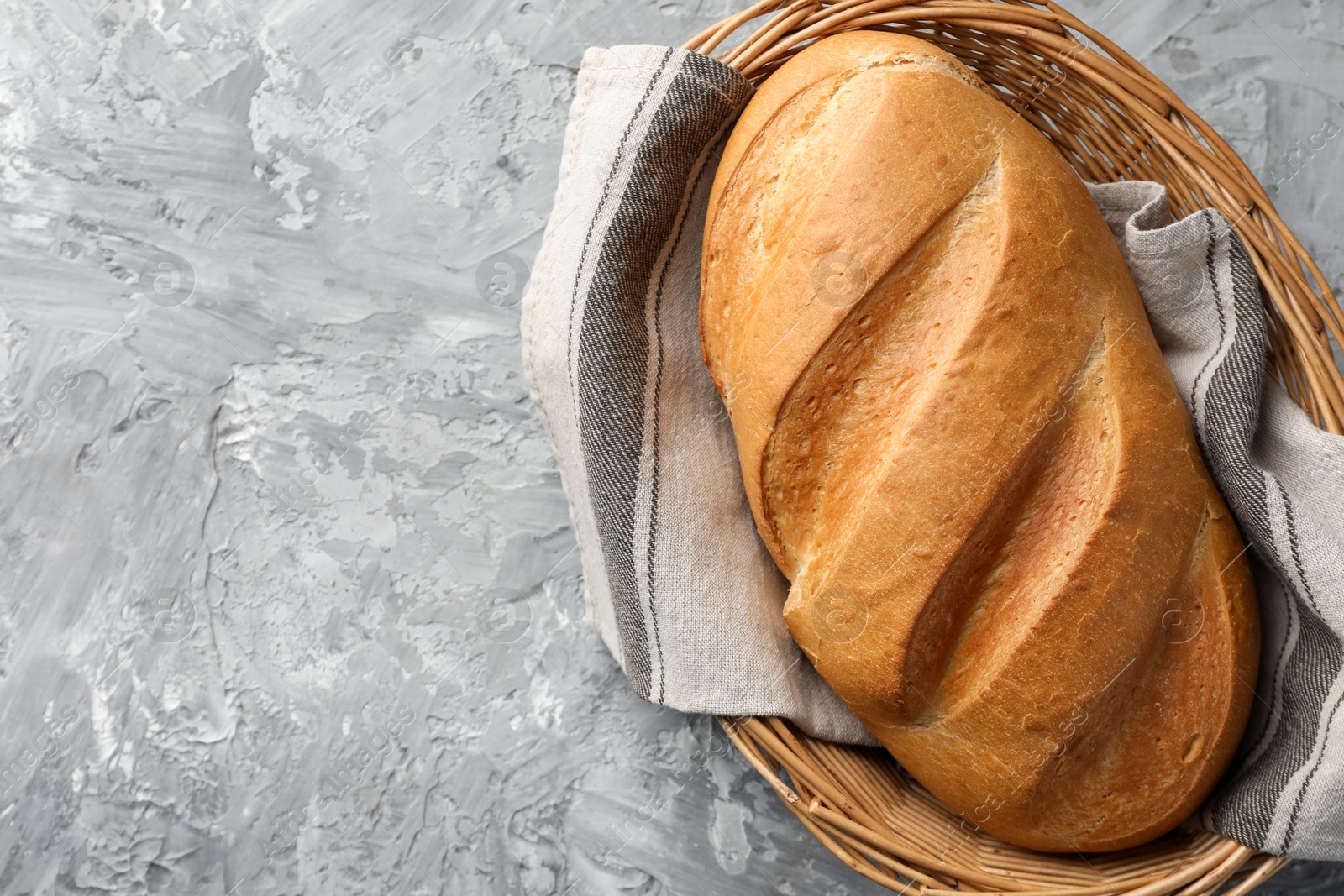 Photo of Freshly baked bread in wicker basket on grey table, top view. Space for text