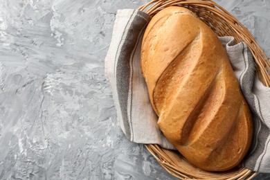 Photo of Freshly baked bread in wicker basket on grey table, top view. Space for text