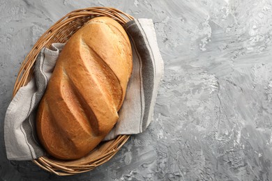 Photo of Freshly baked bread in wicker basket on grey table, top view. Space for text