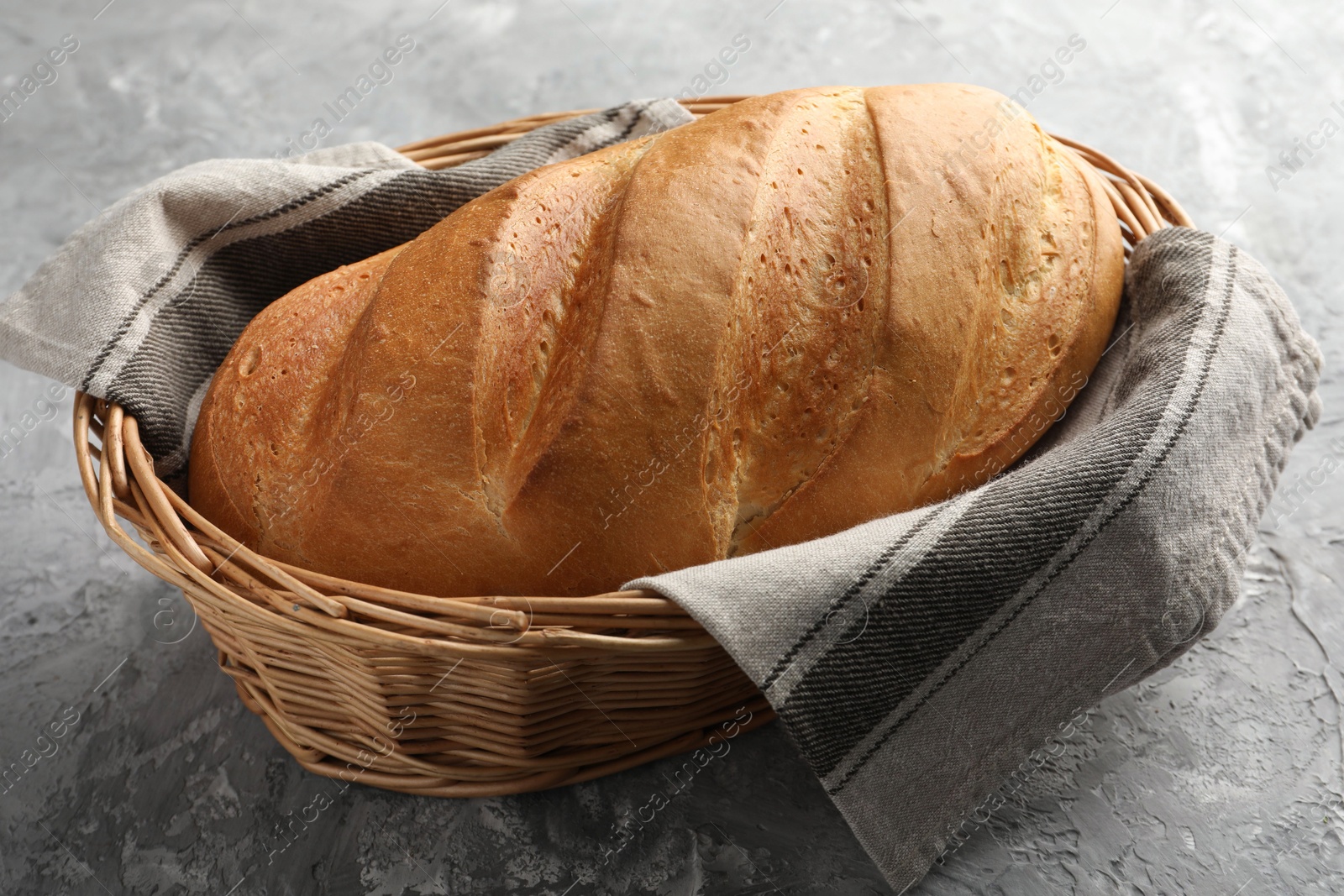 Photo of Freshly baked bread in wicker basket on grey table, closeup