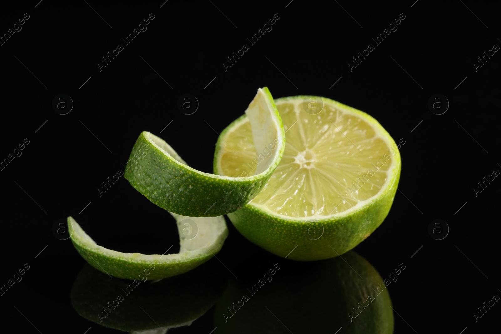 Photo of Fresh lime peel and half of fruit on black glass surface, closeup