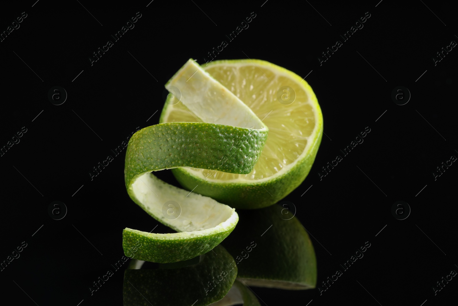 Photo of Fresh lime peel and half of fruit on black glass surface, closeup