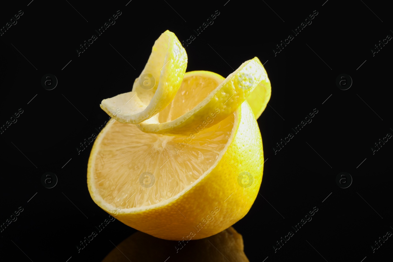 Photo of Fresh lemon peel and half of fruit on black glass surface, closeup