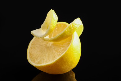 Photo of Fresh lemon peel and half of fruit on black glass surface, closeup