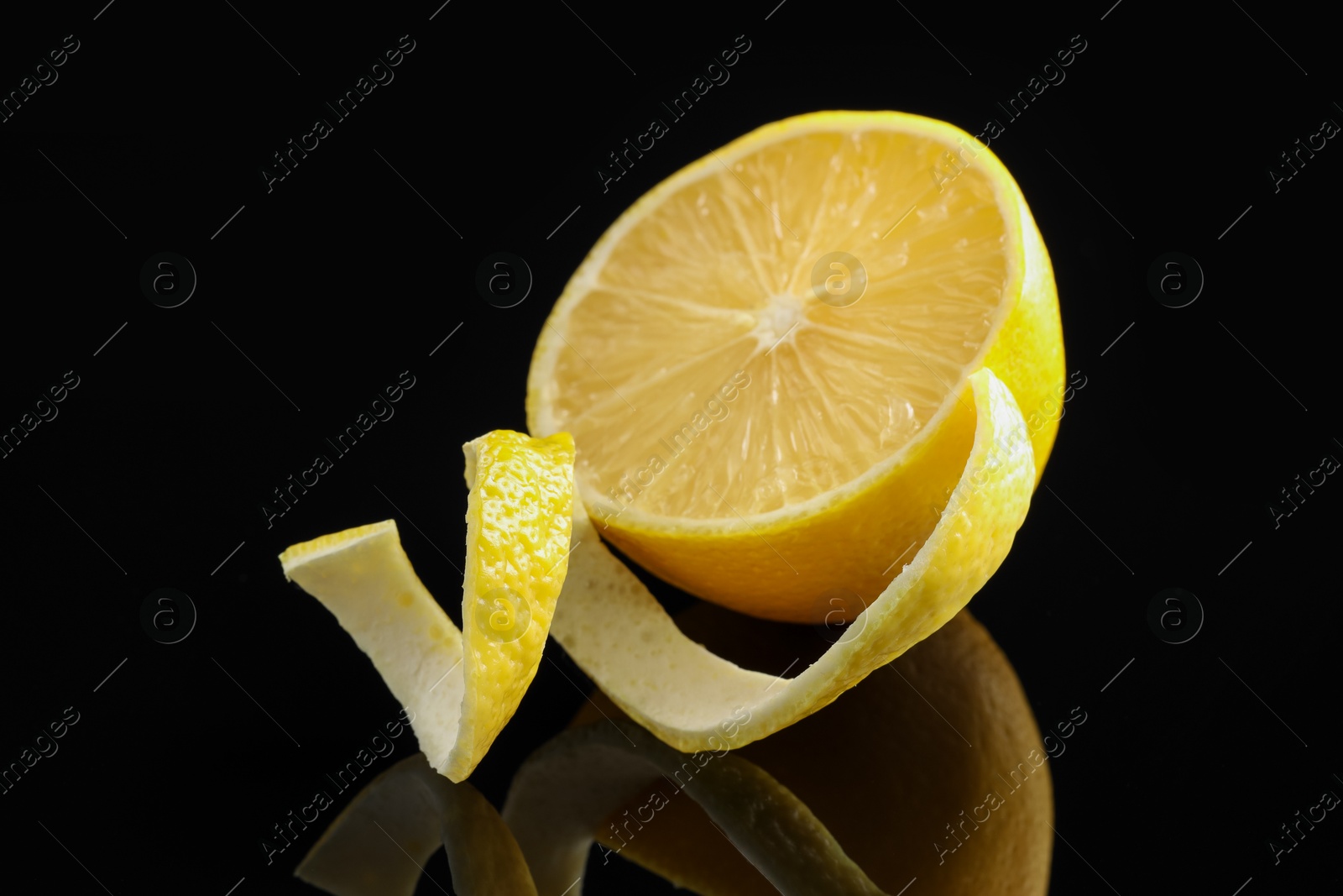 Photo of Fresh lemon peel and half of fruit on black glass surface, closeup