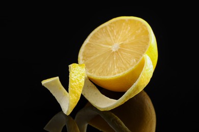 Photo of Fresh lemon peel and half of fruit on black glass surface, closeup