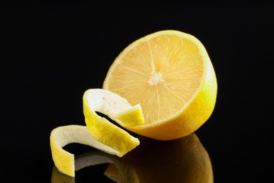 Photo of Fresh lemon peel and half of fruit on black glass surface, closeup