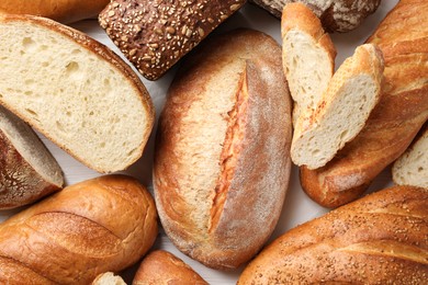 Photo of Whole and cut bread loafs on white table, flat lay