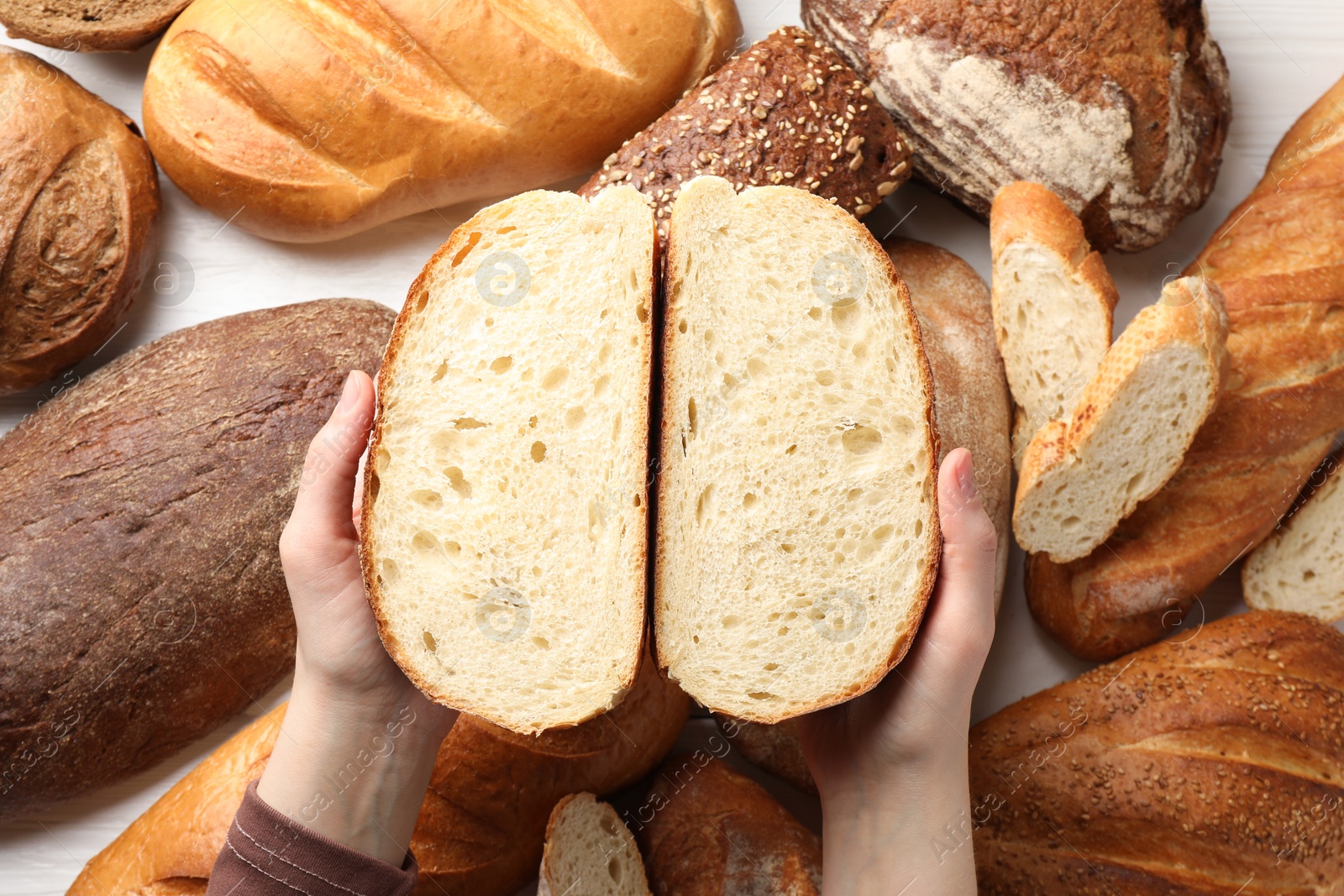 Photo of Woman with pieces of fresh bread over different other loafs at white table, top view