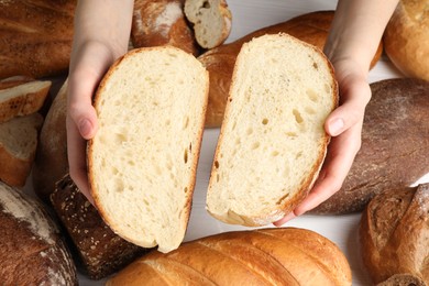 Photo of Woman with pieces of fresh bread over different other loafs at white table, top view