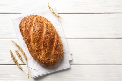 Photo of Loaf of bread with sesame seeds and spikes on white wooden table, flat lay. Space for text