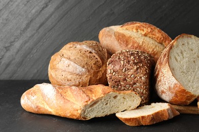 Photo of Whole and cut loafs of bread on black table, closeup