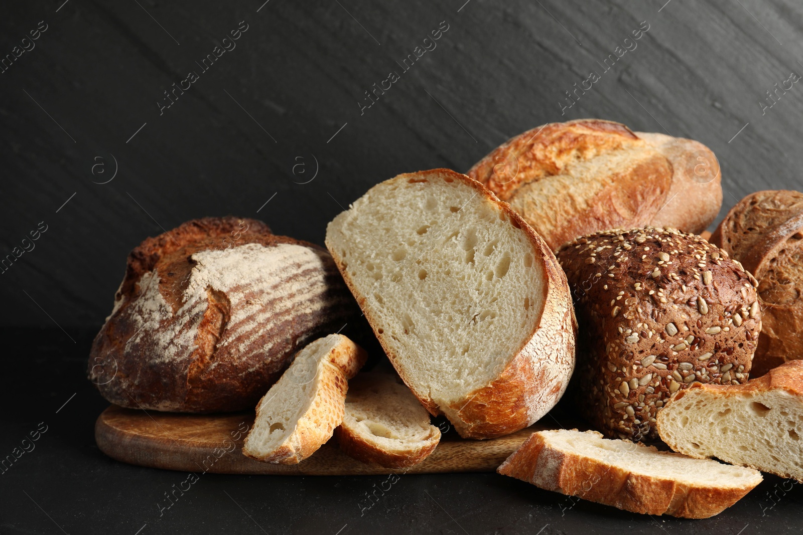 Photo of Whole and cut loafs of bread on black table, closeup