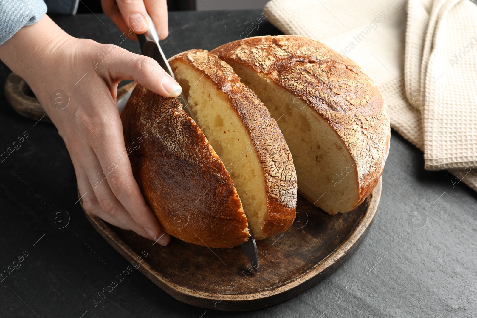 Photo of Woman cutting fresh bread at black table, closeup