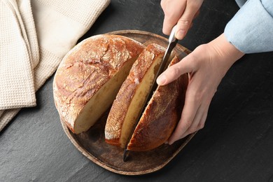 Photo of Woman cutting fresh bread at black table, closeup