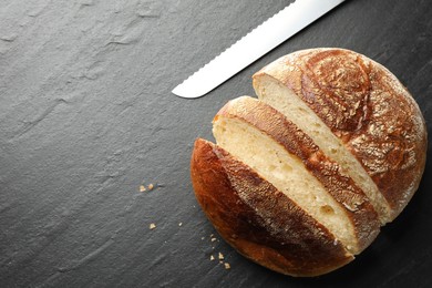 Photo of Cut loaf of fresh bread and knife on black background, top view. Space for text