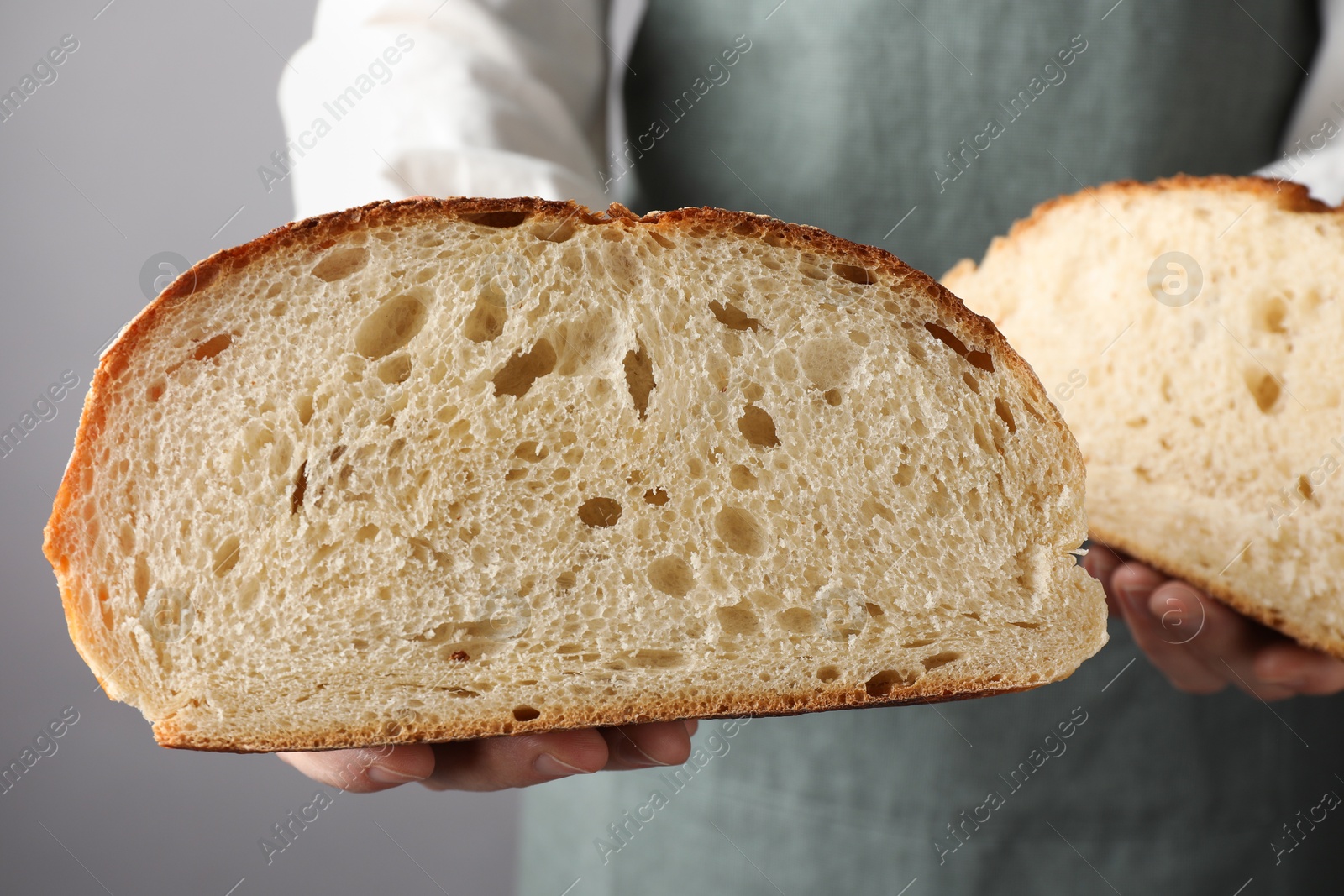 Photo of Woman with pieces of fresh bread on grey background, closeup