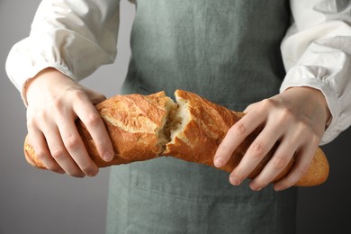 Photo of Woman breaking fresh baguette on grey background, closeup