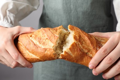 Photo of Woman breaking fresh baguette on grey background, closeup