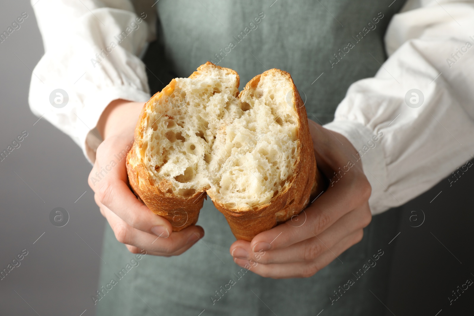 Photo of Woman breaking fresh baguette on grey background, closeup