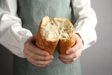 Photo of Woman breaking fresh baguette on grey background, closeup