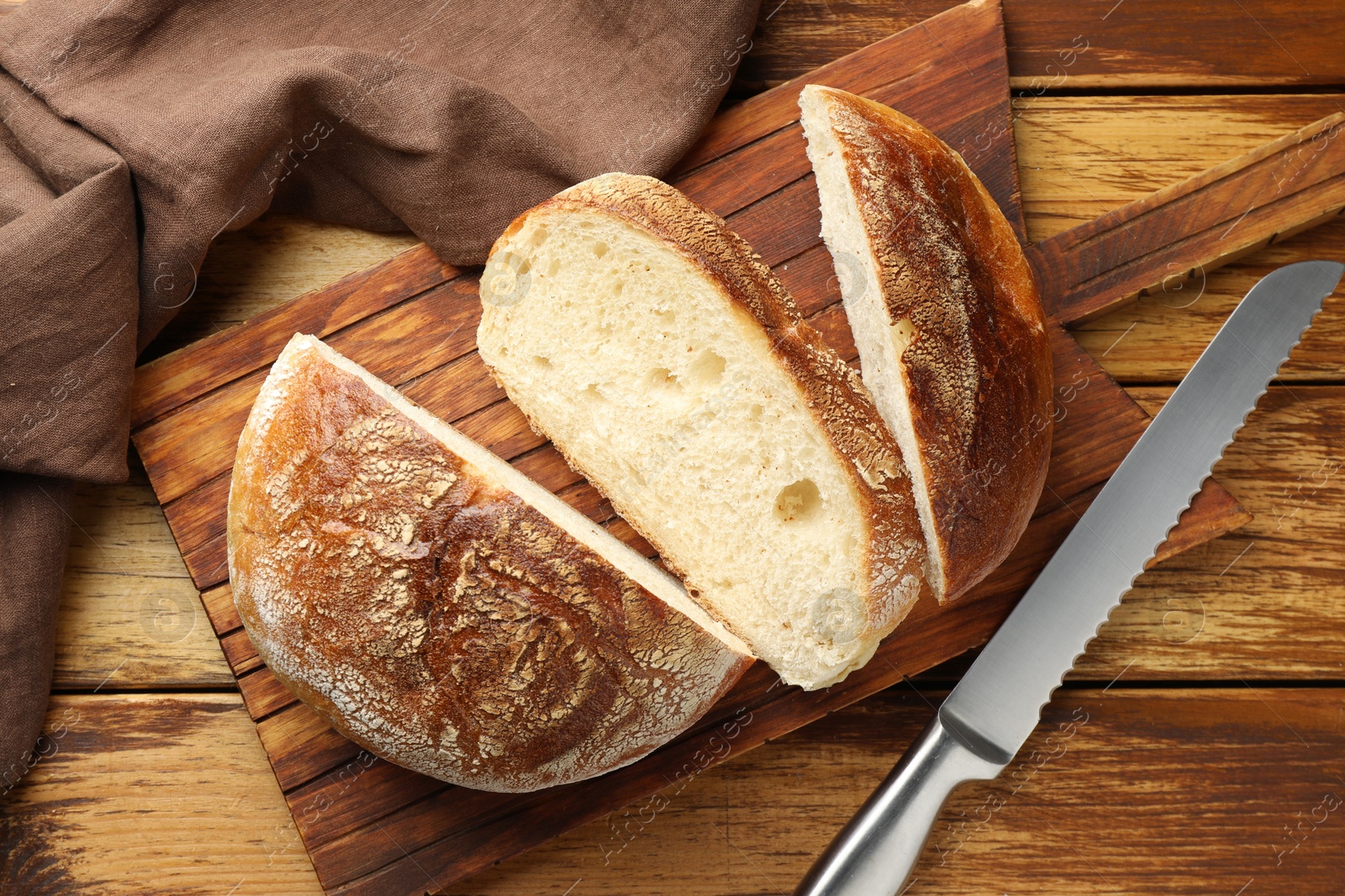 Photo of Cut loaf of fresh bread and knife on wooden table, top view