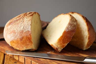 Photo of Cut loaf of fresh bread and knife on wooden table, closeup