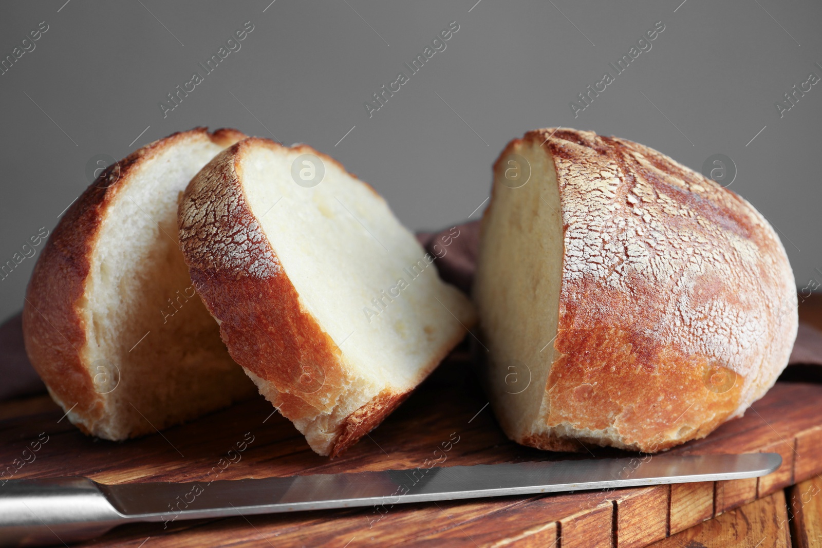 Photo of Cut loaf of fresh bread and knife on wooden table, closeup