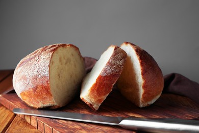 Photo of Cut loaf of fresh bread and knife on wooden table, closeup