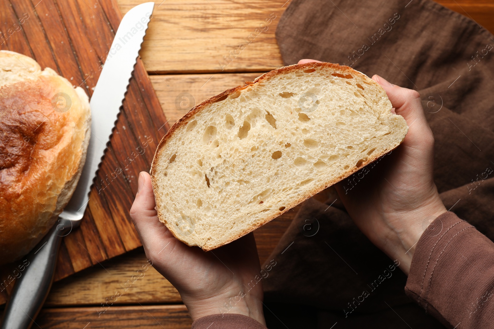 Photo of Woman with piece of fresh bread at wooden table, top view