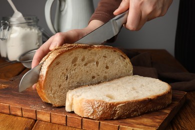 Photo of Woman cutting freshly baked bread at wooden table, closeup