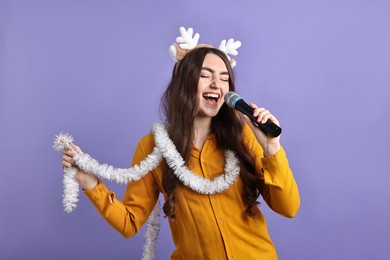 Photo of Young woman in reindeer headband with tinsel singing on purple background