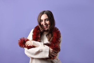 Photo of Happy young woman with tinsel on purple background