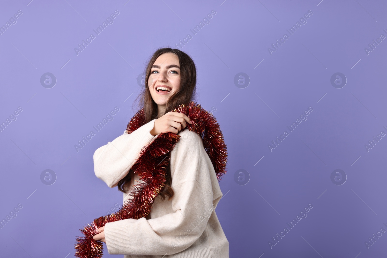 Photo of Happy young woman with tinsel on purple background