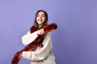 Photo of Happy young woman with tinsel on purple background. Space for text