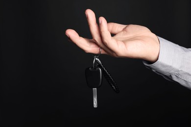 Photo of Man with car key and keychain on black background, closeup. Space for text