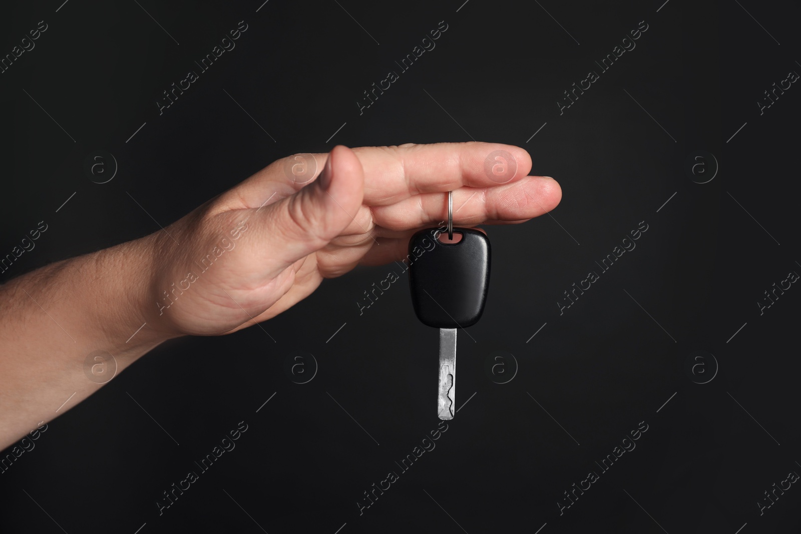 Man with car key on black background, closeup Photo of Man with car key on black background, closeup