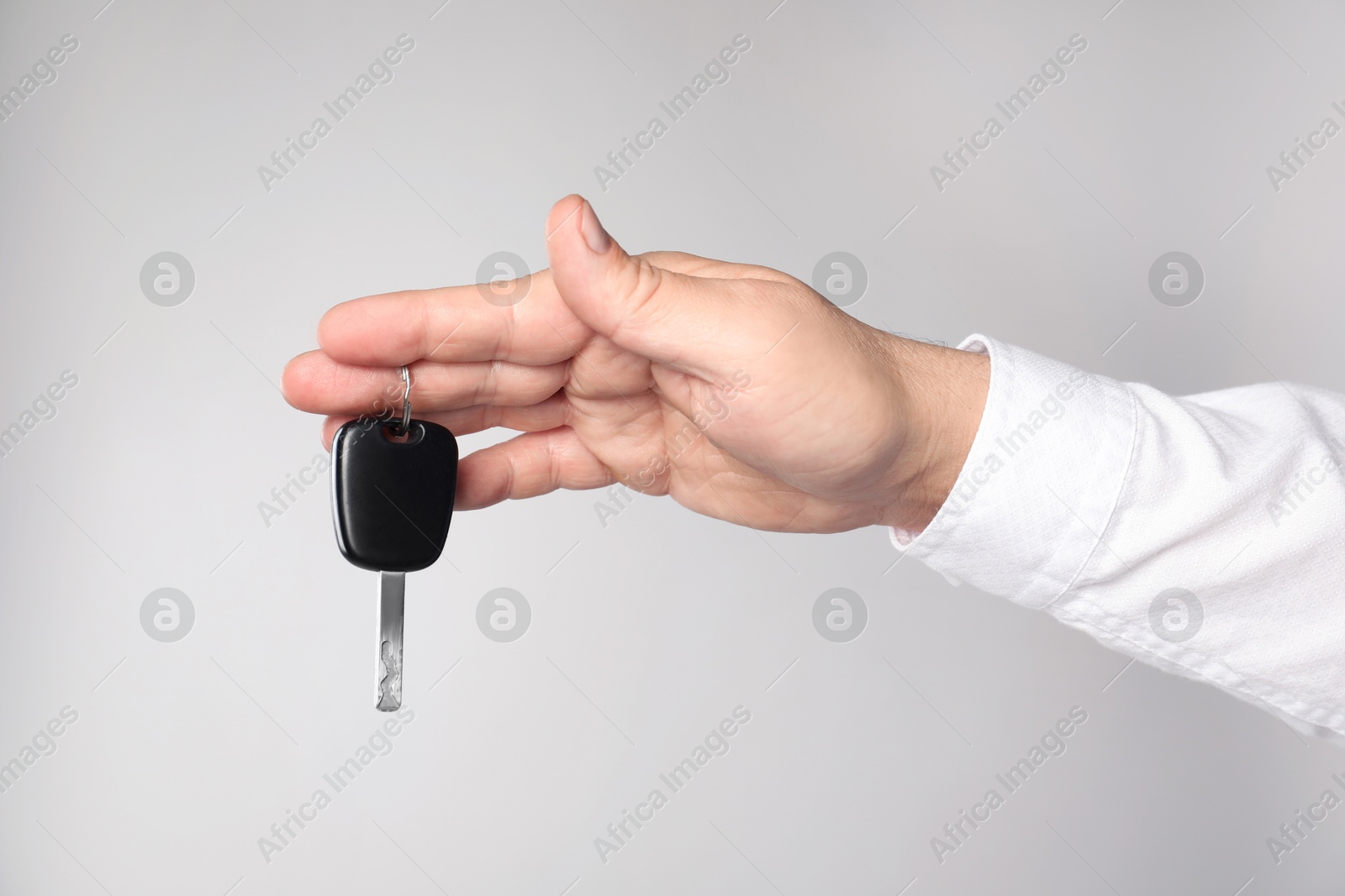 Man with car key on light grey background, closeup Photo of Man with car key on light grey background, closeup