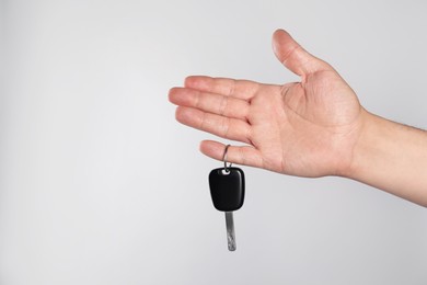 Man with car key on light grey background, closeup. Space for text