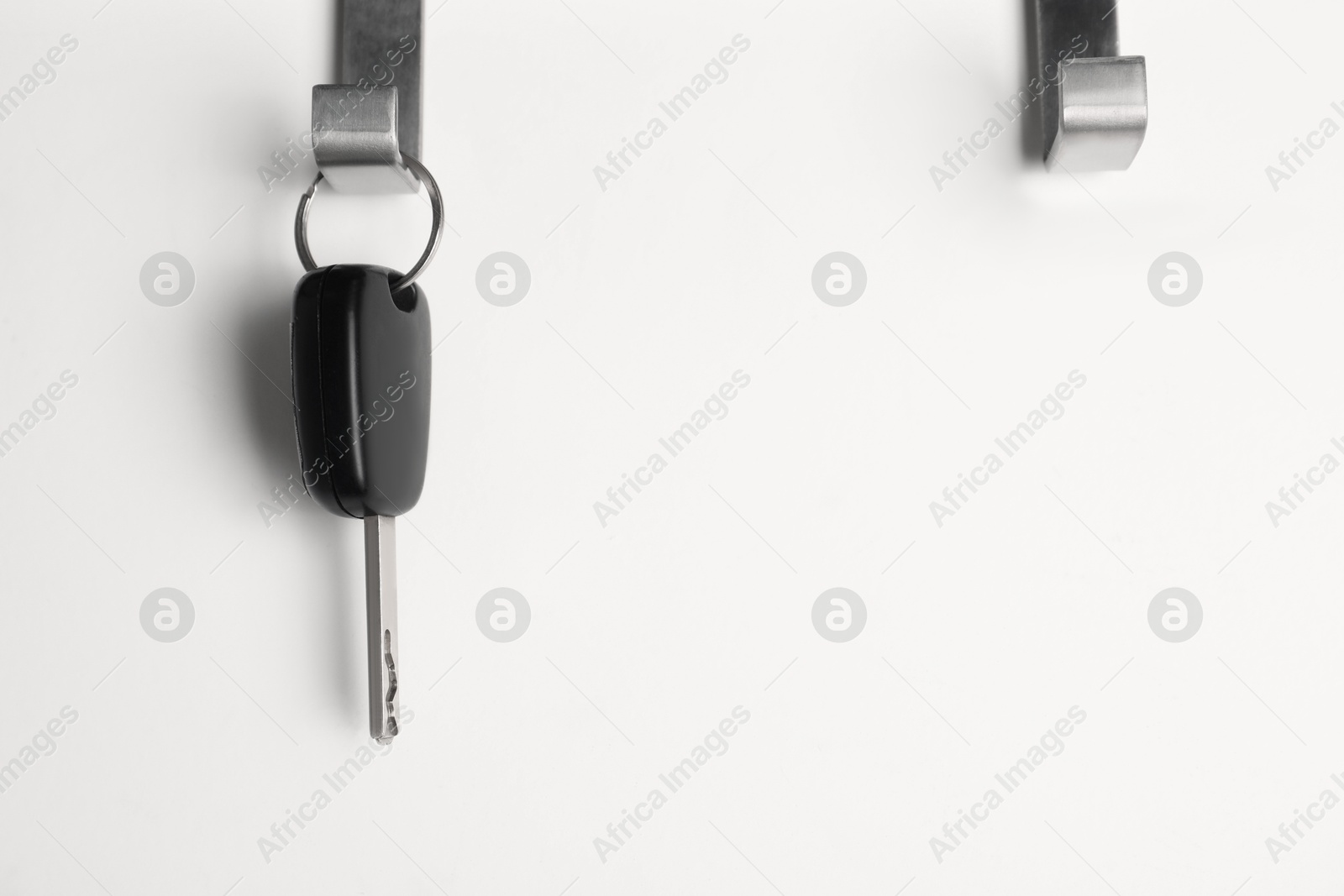 Photo of Car key hanging on light wall, space for text