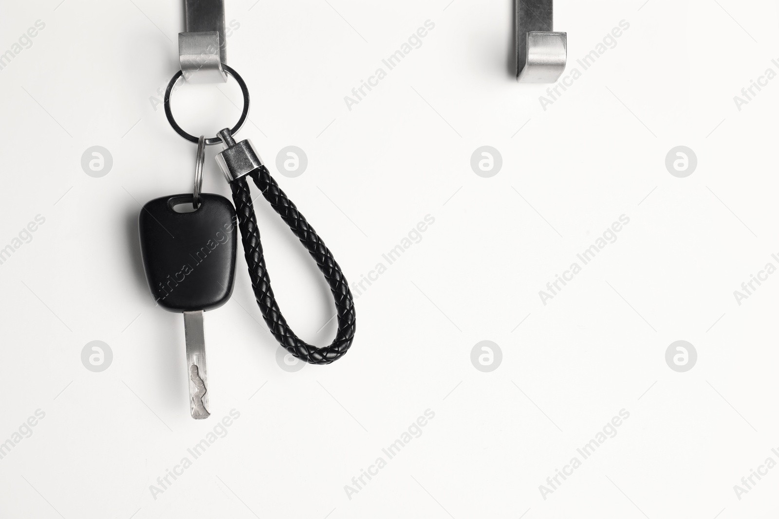 Photo of Car key hanging on light wall, space for text