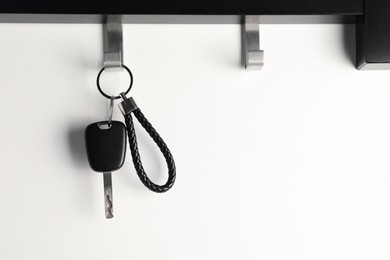 Photo of Car key hanging on light wall, space for text