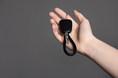 Photo of Woman with car key and keychain on grey background, closeup. Space for text