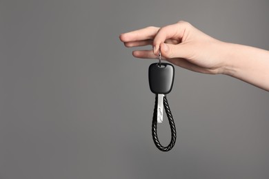 Photo of Woman with car key and keychain on grey background, closeup. Space for text