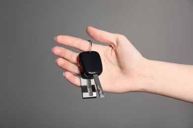 Photo of Woman with car key and keychain on grey background, closeup