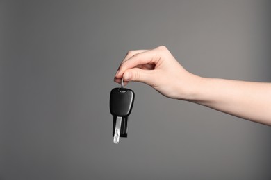 Photo of Woman with car key and keychain on grey background, closeup. Space for text