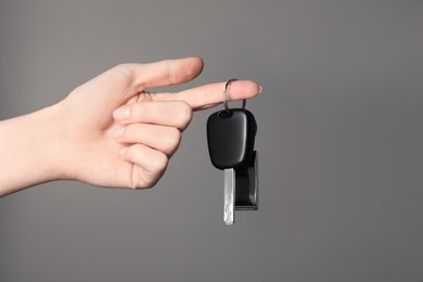 Photo of Woman with car key and keychain on grey background, closeup. Space for text