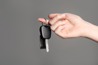 Photo of Woman with car key and keychain on grey background, closeup. Space for text