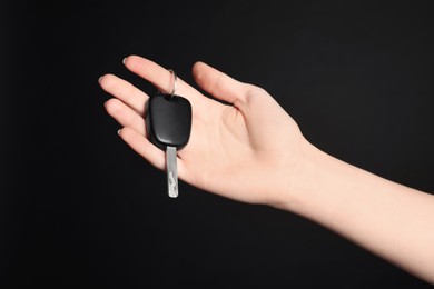 Woman with car key on black background, closeup